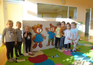 Grupa dzieci stoi wokół foto budki z misiami.